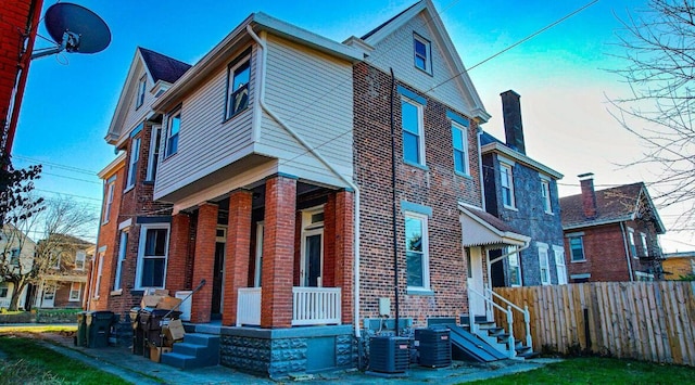 view of front facade with fence, cooling unit, a porch, and brick siding
