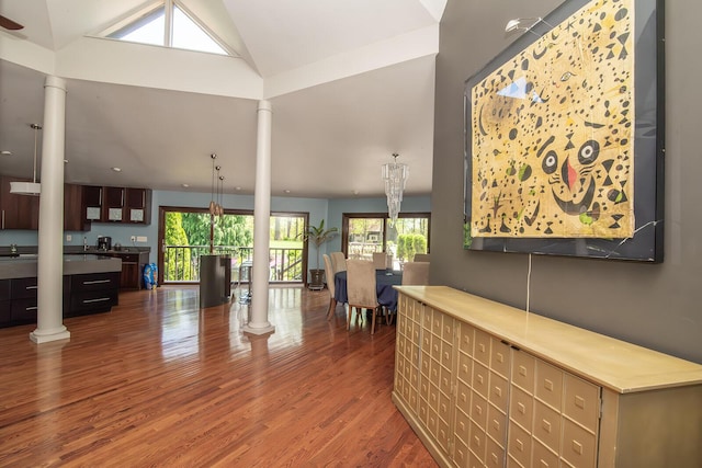 living area featuring decorative columns, wood finished floors, and lofted ceiling