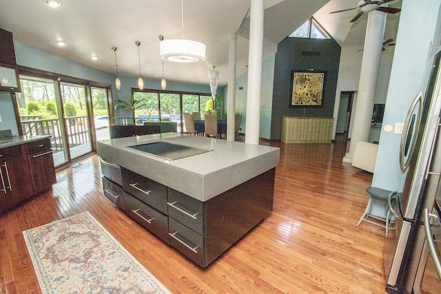 kitchen with light wood-type flooring, a ceiling fan, a towering ceiling, and decorative light fixtures