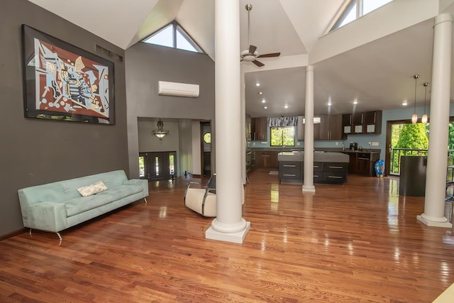 living room with ornate columns, ceiling fan, wood finished floors, and high vaulted ceiling