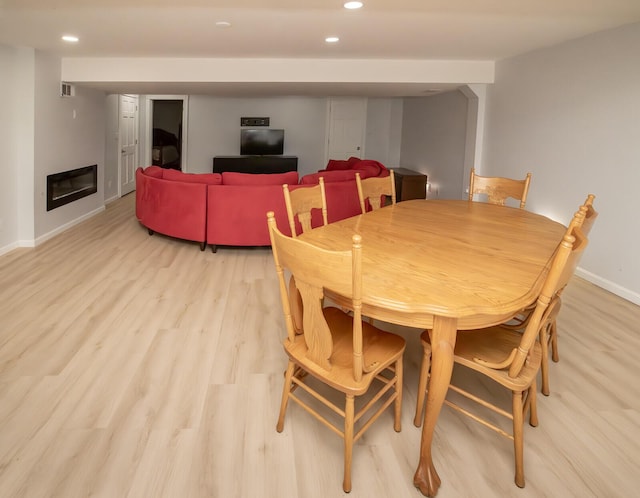 dining space with a glass covered fireplace, light wood-style flooring, recessed lighting, baseboards, and visible vents