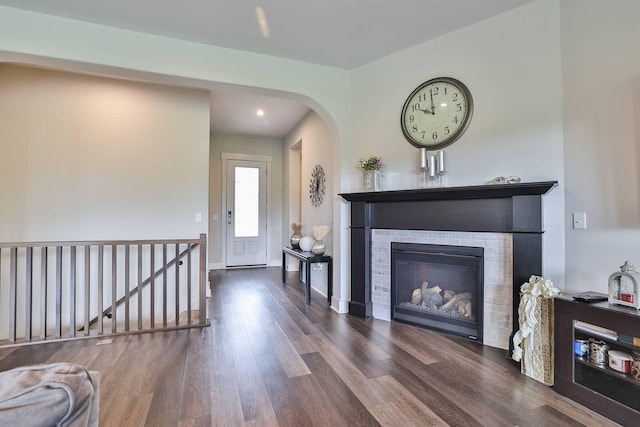 living area with recessed lighting, arched walkways, a brick fireplace, and wood finished floors
