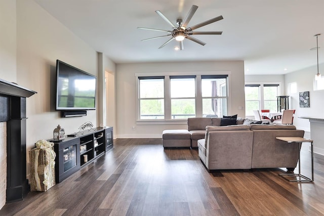 living area featuring baseboards, a ceiling fan, dark wood finished floors, and a healthy amount of sunlight