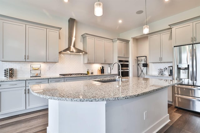 kitchen featuring wall chimney range hood, appliances with stainless steel finishes, a sink, backsplash, and gray cabinetry