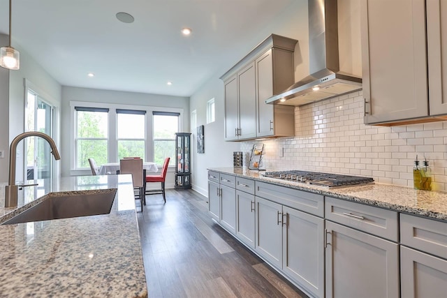 kitchen with gray cabinets, a sink, dark wood-style floors, stainless steel gas stovetop, and wall chimney exhaust hood