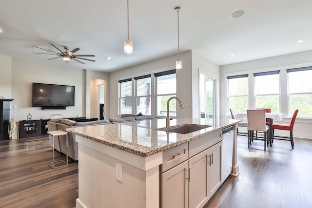kitchen featuring dark wood-style flooring, hanging light fixtures, a center island with sink, a sink, and dishwashing machine