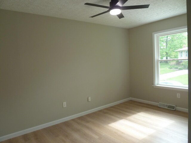 spare room featuring ceiling fan, plenty of natural light, a textured ceiling, visible vents, and light wood-style floors