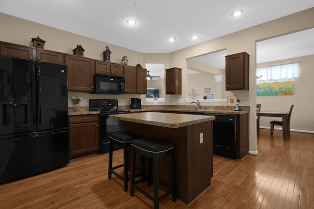 kitchen with a center island, light wood finished floors, black appliances, and dark brown cabinets