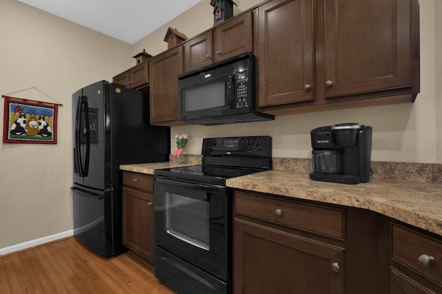 kitchen featuring dark brown cabinets, baseboards, light countertops, light wood finished floors, and black appliances