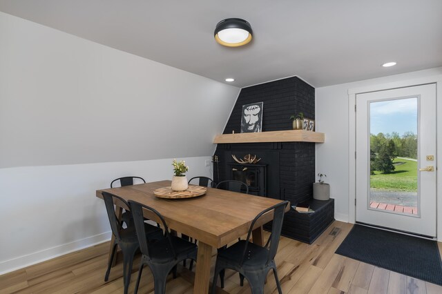 dining space with light wood-style floors, a brick fireplace, lofted ceiling, baseboards, and recessed lighting