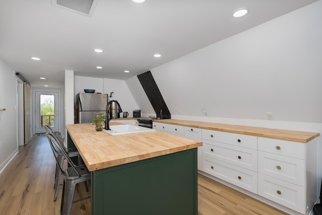 kitchen with wooden counters, freestanding refrigerator, a sink, white cabinets, and recessed lighting