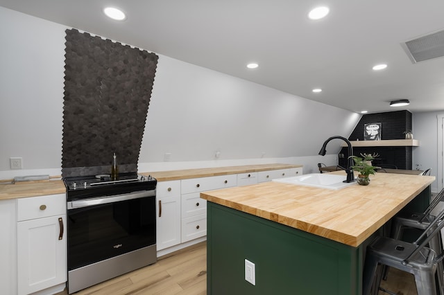 kitchen featuring butcher block counters, stainless steel range with electric stovetop, a sink, light wood-style flooring, and white cabinets
