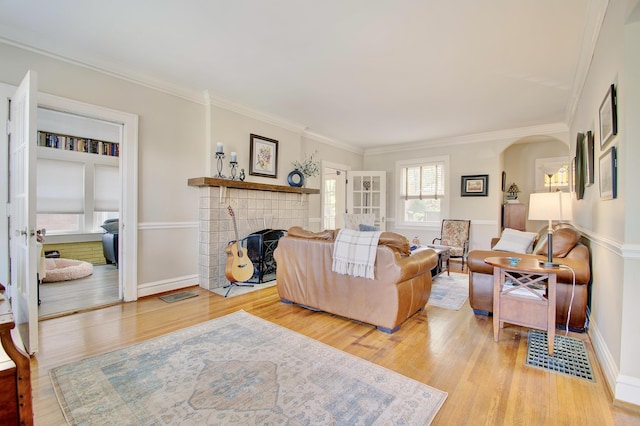 living area featuring visible vents, a fireplace, baseboards, light wood finished floors, and ornamental molding