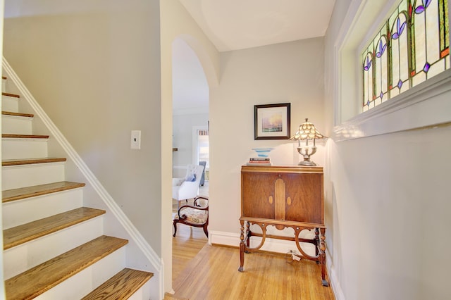 staircase with baseboards, arched walkways, and wood finished floors
