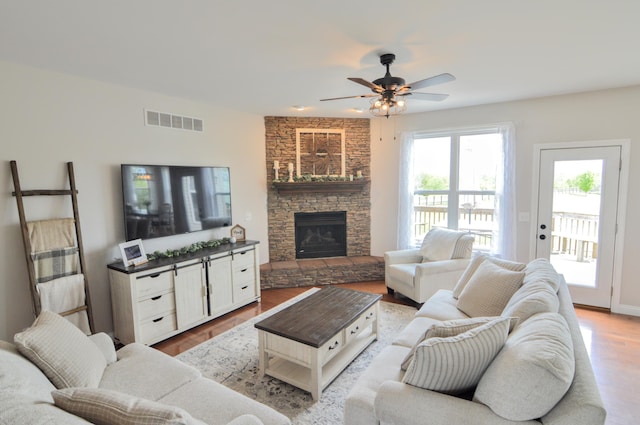 living area featuring ceiling fan, visible vents, a stone fireplace, and wood finished floors