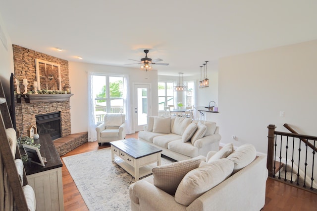 living room with a stone fireplace, a ceiling fan, and wood finished floors