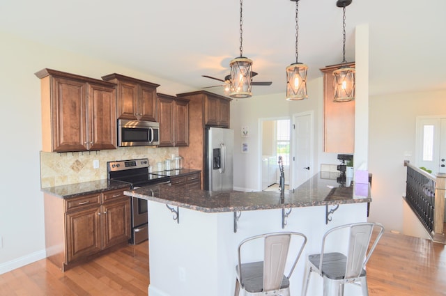 kitchen featuring a breakfast bar, stainless steel appliances, a ceiling fan, light wood-type flooring, and tasteful backsplash