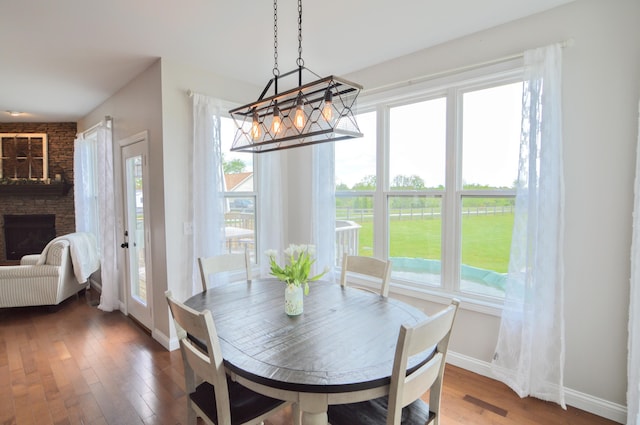dining space with baseboards, wood finished floors, a notable chandelier, and a stone fireplace