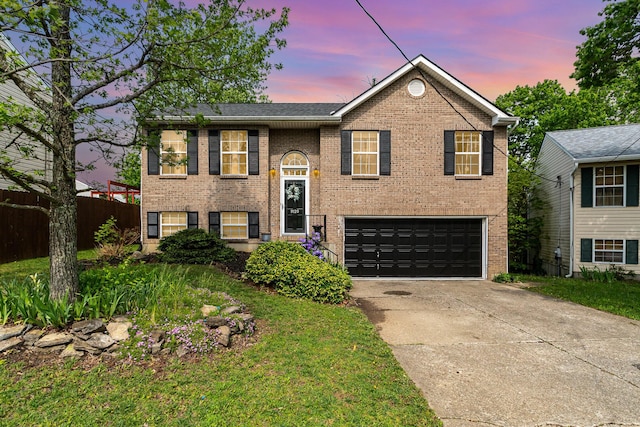 raised ranch featuring concrete driveway, brick siding, an attached garage, and fence