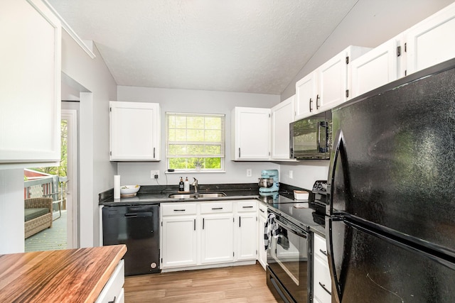 kitchen featuring dark countertops, light wood-type flooring, a sink, white cabinets, and black appliances