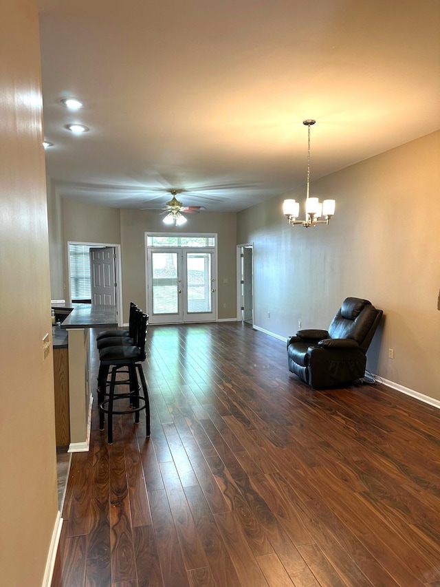living area with baseboards, dark wood-style flooring, and ceiling fan with notable chandelier