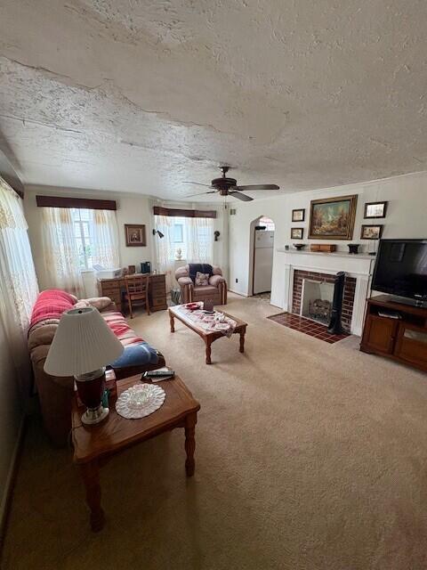living room with a ceiling fan, a textured ceiling, a fireplace with flush hearth, arched walkways, and light carpet