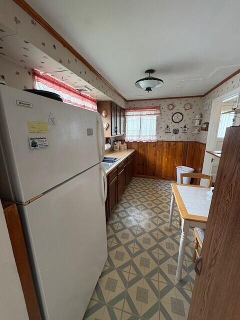 kitchen featuring wooden walls, a wainscoted wall, freestanding refrigerator, wallpapered walls, and light floors