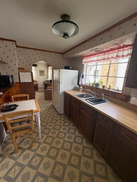 kitchen featuring black microwave, a sink, arched walkways, wallpapered walls, and light floors