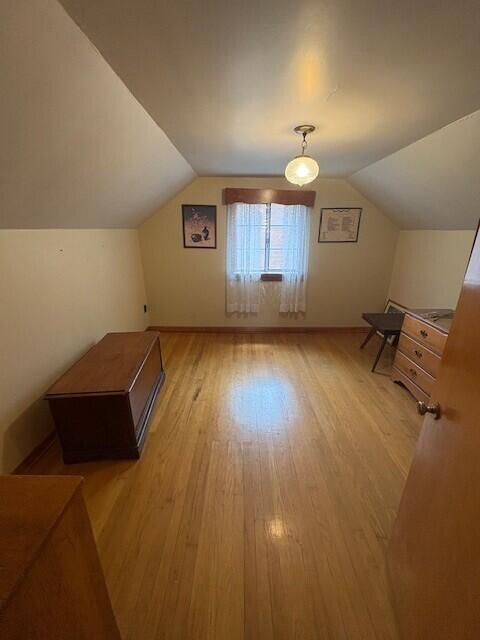 additional living space featuring baseboards, vaulted ceiling, and light wood-type flooring