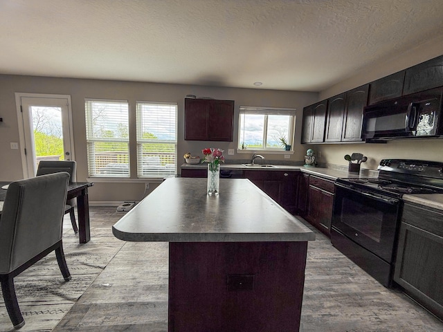 kitchen featuring black appliances, a sink, light wood-type flooring, a center island, and a textured ceiling