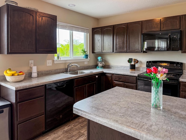 kitchen with black appliances, a sink, dark brown cabinets, wood finished floors, and light countertops