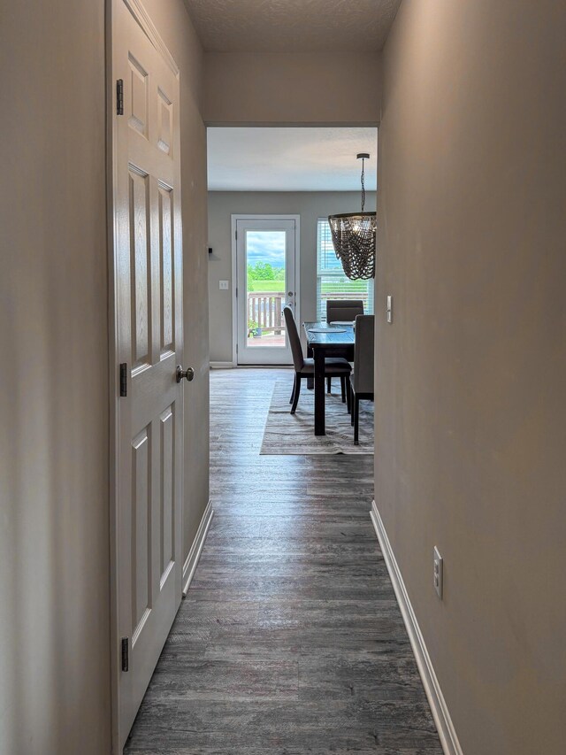 hall with a chandelier, dark wood finished floors, and baseboards