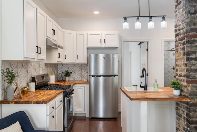 kitchen featuring butcher block counters, under cabinet range hood, white cabinets, backsplash, and stainless steel appliances