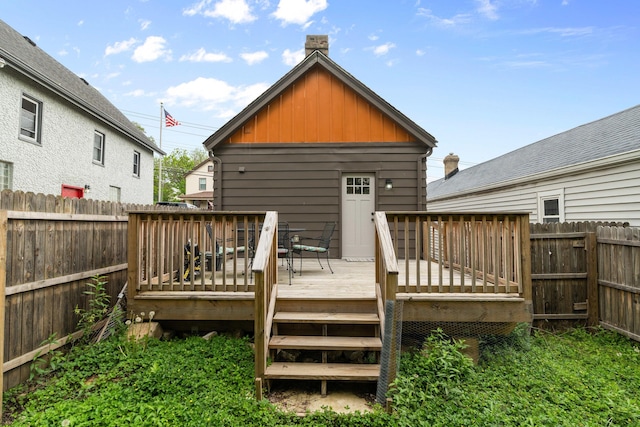 back of house featuring board and batten siding, a wooden deck, a fenced backyard, and a chimney