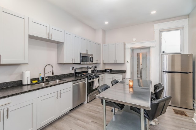 kitchen with dark stone counters, appliances with stainless steel finishes, a sink, and light wood-style floors