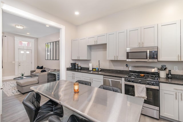 kitchen with a kitchen bar, dark countertops, a sink, stainless steel appliances, and light wood-style flooring