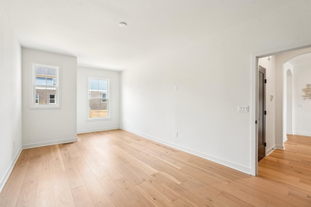 empty room featuring arched walkways, light wood-style flooring, and baseboards