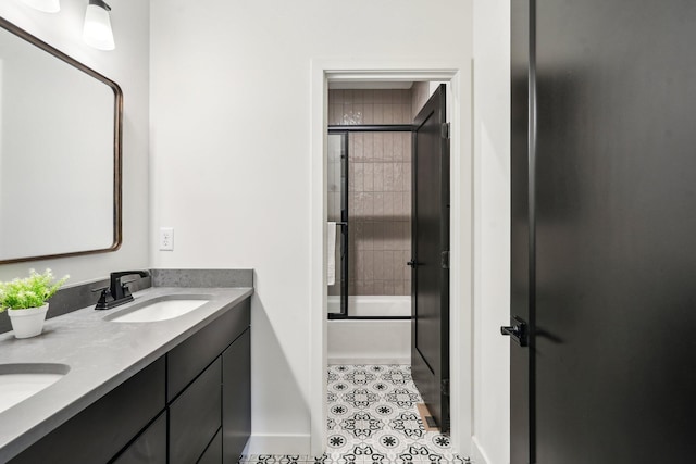 bathroom featuring double vanity, tile patterned flooring, baseboards, and combined bath / shower with glass door