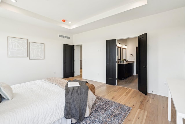 bedroom featuring light wood-type flooring, recessed lighting, a raised ceiling, baseboards, and ensuite bath