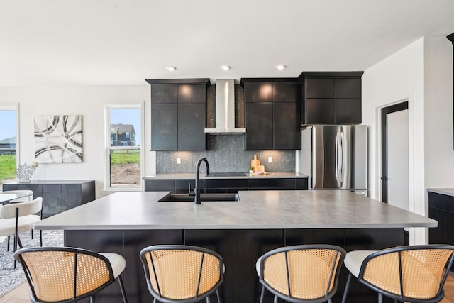 kitchen featuring wall chimney range hood, a sink, freestanding refrigerator, and healthy amount of natural light