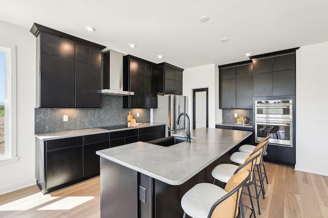 kitchen with wall chimney range hood, modern cabinets, a breakfast bar, stainless steel appliances, and recessed lighting