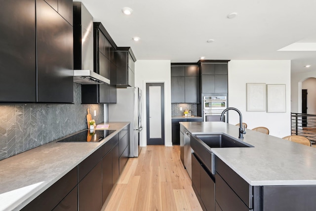 kitchen with stainless steel appliances, a center island with sink, light wood finished floors, a sink, and modern cabinets