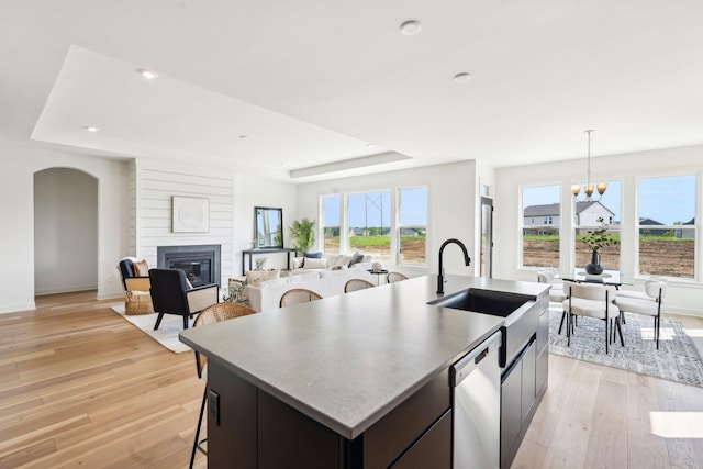 kitchen with a sink, dishwasher, a kitchen island with sink, a tray ceiling, and a glass covered fireplace