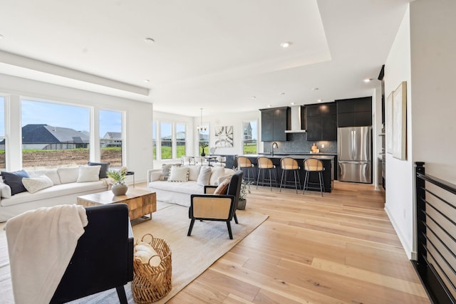 living room with a raised ceiling, light wood-style floors, and recessed lighting