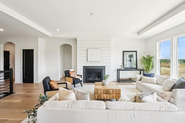 living area featuring arched walkways, light wood-type flooring, baseboards, a large fireplace, and recessed lighting