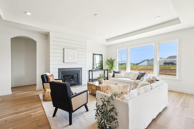 living room with a raised ceiling, baseboards, a glass covered fireplace, light wood-type flooring, and recessed lighting