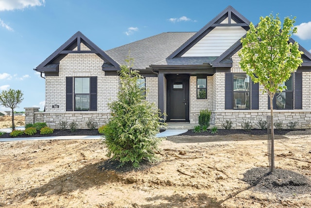 view of front of house featuring brick siding, a shingled roof, and stone siding