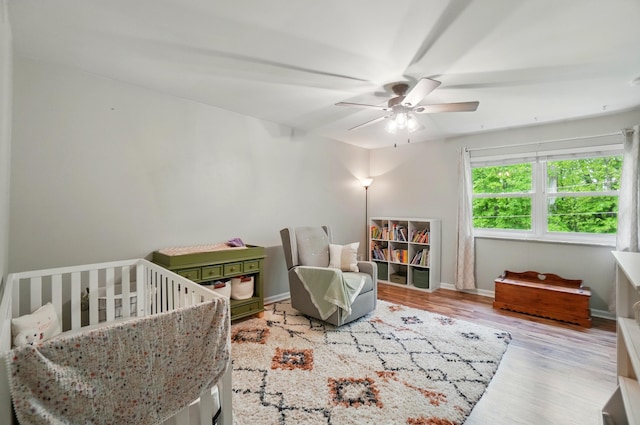 bedroom with wood finished floors, a crib, a ceiling fan, and baseboards