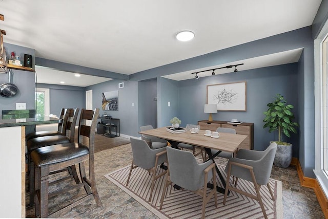 dining area with stone finish floors, baseboards, and rail lighting