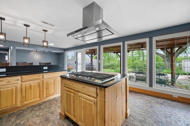 kitchen featuring ventilation hood, stainless steel gas stovetop, dark stone finish floors, decorative light fixtures, and a kitchen island